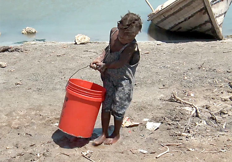 Young child struggles to carry water.