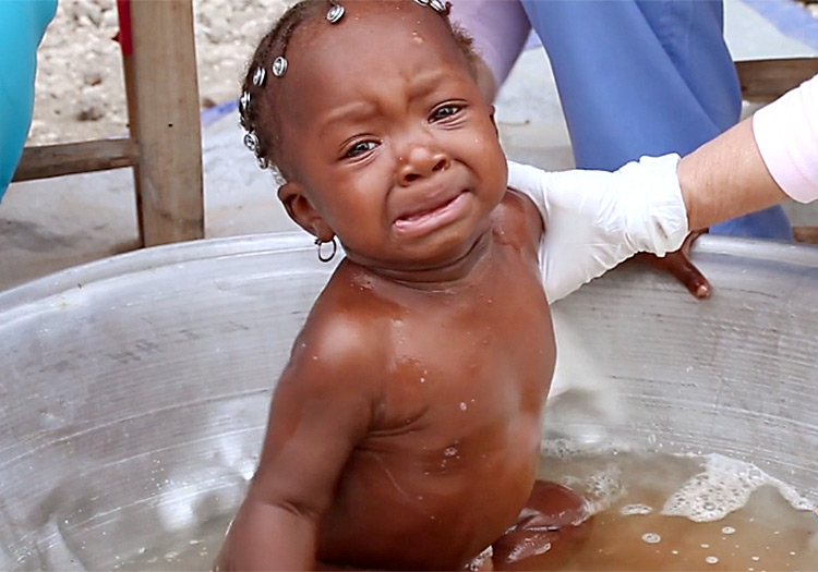Crying baby gets medicinal bath.