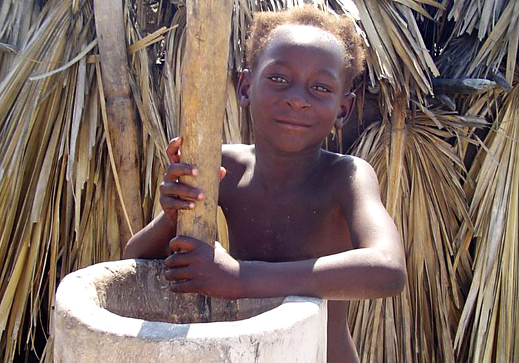 Haitian girl grinding corn in a pylon