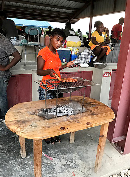 Haitian woman cooking hot dogs at the marketplace.