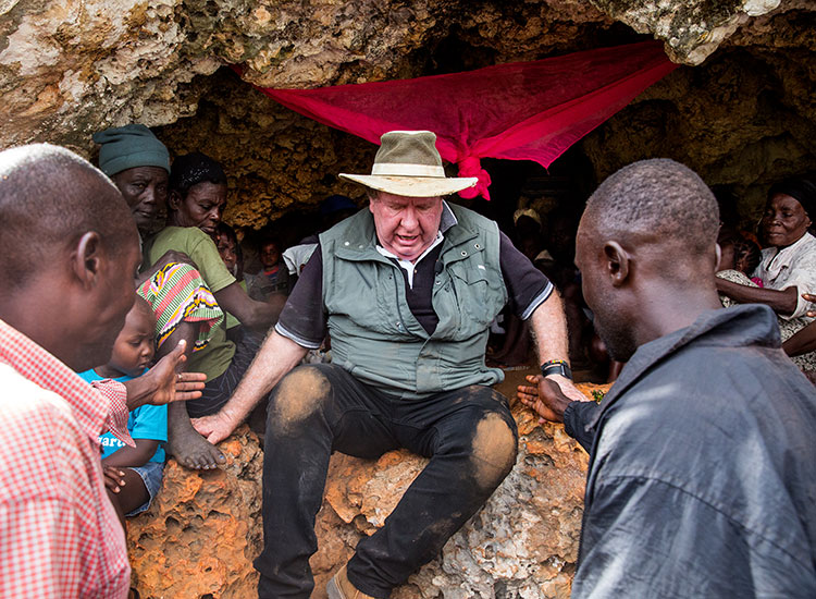 Bobby crawls out the cave with the help of some Haitian men