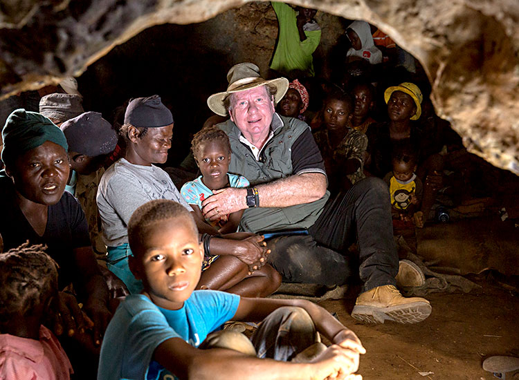 Bobby sits with poor Haitian familes inside a cave