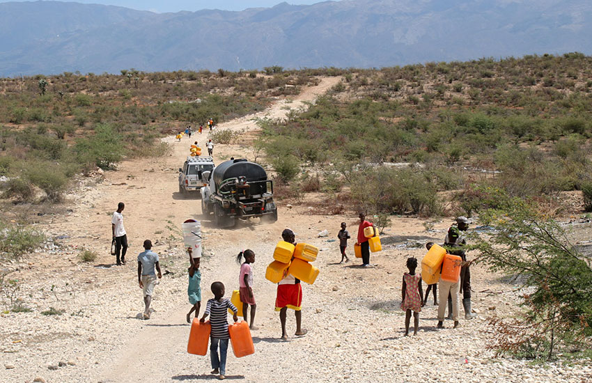 Children following the water truck and hope to fill up all their water containers to carry back home.